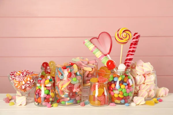 ピンクを背景にした白い木製のテーブルの上に異なるおいしいキャンディーを持つ瓶 — ストック写真