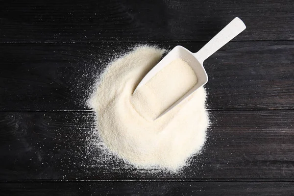 Pile of gelatin powder and scoop on black wooden table, top view