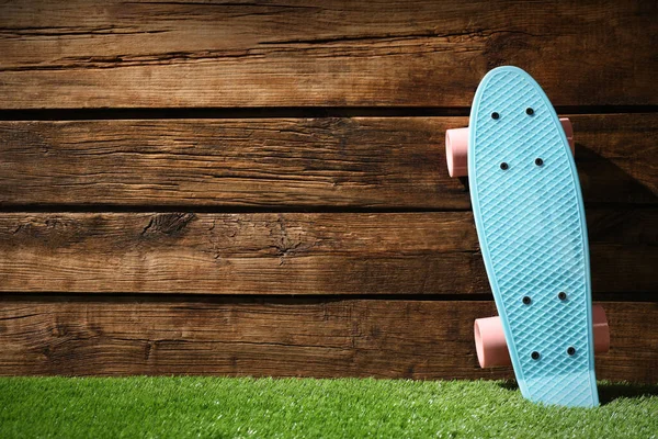 木製の壁の近くの緑の芝生の上にピンクの車輪とライトブルーのスケートボード テキストのためのスペース — ストック写真