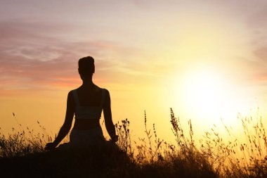 Gün batımında dışarıda meditasyon yapan bir kadın silueti. Metin için boşluk