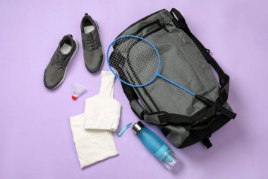 Gri spor çantası ve menekşe arka planda badminton ekipmanı.