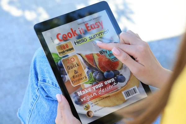 Woman reading online magazine on tablet outdoors, closeup