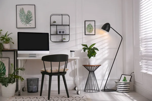 Comfortable workplace with modern computer and houseplants in room. Interior design