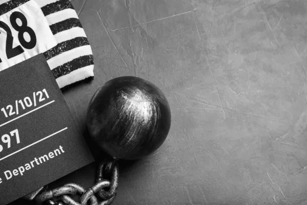 Metal ball with chain, prison uniform and mugshot letter board on grey table, flat lay. Space for text