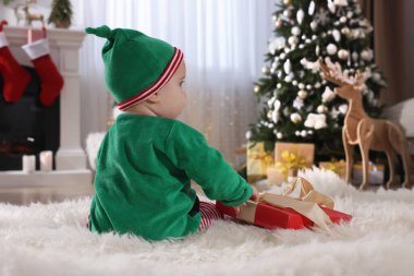 Noel hediyesinin yanında şirin elf kostümlü bebek. Evde yerde, arka manzara.