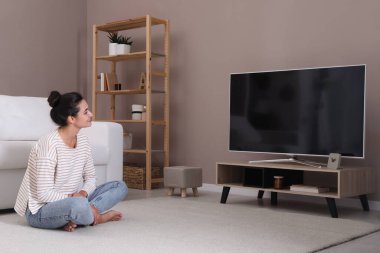 Evde televizyon izleyen bir kadın. Oturma odasının içinde televizyon var.