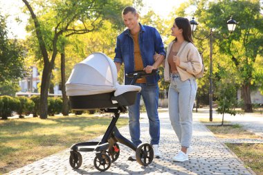 Mutlu ebeveynler güneşli bir günde bebekleriyle parkta yürüyorlar.
