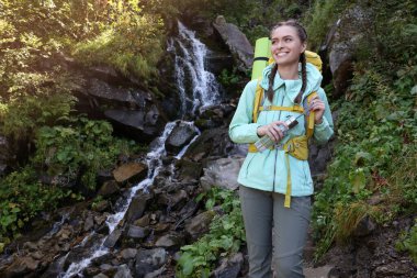 Dağlarda şelale yakınında sırt çantası ve şişe taşıyan bir turist. Metin için boşluk