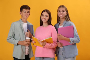 Sarı arka planda kırtasiyesi olan bir grup genç öğrenci.