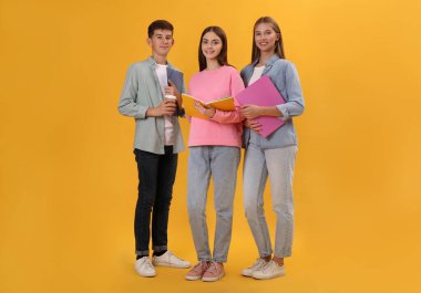 Sarı arka planda kırtasiyesi olan bir grup genç öğrenci.