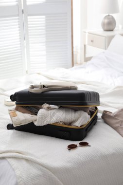 Odada elbise, ceket ve şık aksesuarlarla dolu bir bavul var.