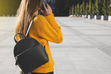 Havalı siyah sırt çantalı genç bir kadın dışarıda telefonla konuşuyor, yakın plan. Metin için boşluk