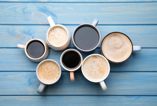 Many cups of different coffee drinks on light blue wooden table, flat lay