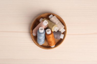 Ahşap masa üzerinde renkli dikiş iplikleri olan bir kase, üst manzara.