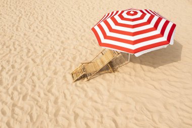 Kumlu sahilde tahta güneş yatağının yanındaki çizgili plaj şemsiyesi