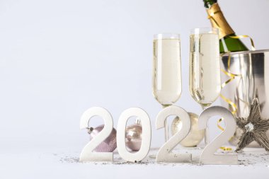 Mutlu yıllar 2022! Kovada bir şişe köpüklü şarap ve beyaz arka planda bardaklar