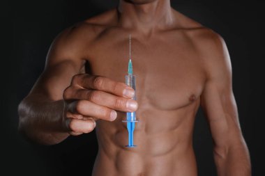 Siyah arka planda şırıngası olan atletik bir adam, yakın plan. Doping kavramı