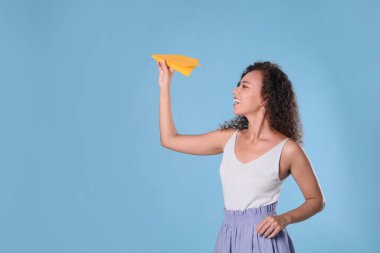 Güzel bir Afro-Amerikalı kadın açık mavi arka planda kağıt uçakla oynuyor. Metin için boşluk