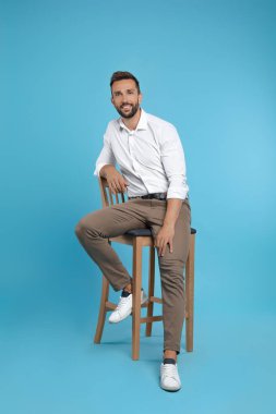 Turkuaz arka planda iskemlede oturan yakışıklı adam.