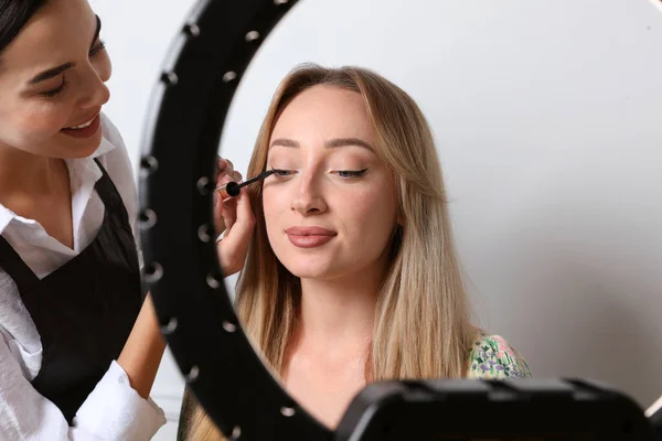Profesjonalny Makijaż Artysta Pracuje Piękną Młodą Kobietą Lekkim Tle Widok — Zdjęcie stockowe