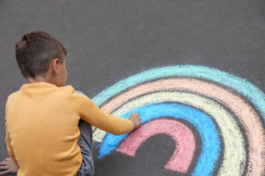 Gökkuşağını asfaltta tebeşirle çizen çocuk.