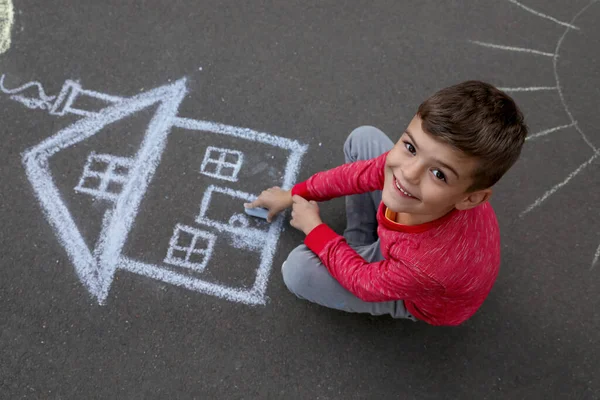 Child drawing house with chalk on asphalt, above view
