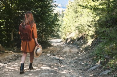 Sırt çantalı ve şapkalı bir kadın ormanda yürüyor.