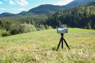 Açık havada tripoda yerleştirilmiş akıllı telefonlu güzel dağ manzarasının fotoğrafını çekiyoruz.