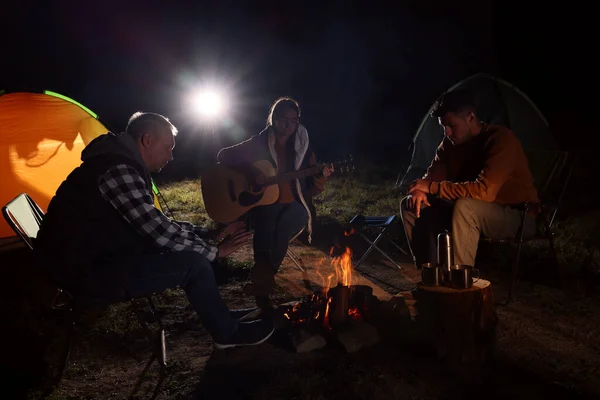 たき火の近くにギターを持つ友人のグループとキャンプテントの屋外で夜 — ストック写真