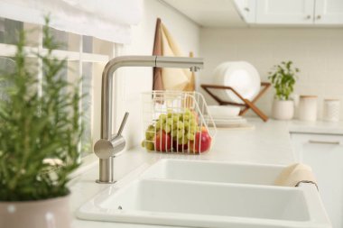 Mutfak penceresinin yanında musluğu olan beyaz lavabo. İç tasarım