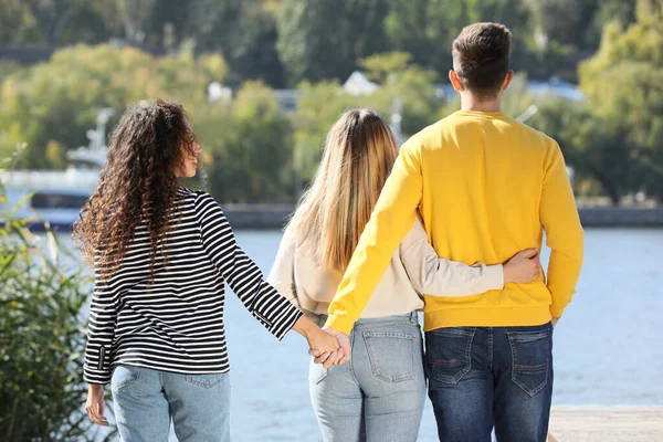 Man holding hands with another woman behind his girlfriend\'s back near river on sunny day. Love triangle