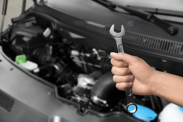 Auto mechanic with wrench near broken down car, closeup