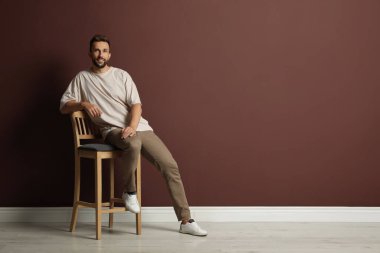 Kahverengi duvarın yanındaki taburede oturan yakışıklı adam. Metin için boşluk