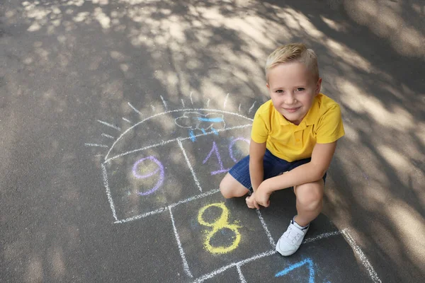 屋外アスファルトの上にチョークでホプスコッチを描く小さな男の子 幸せな子供時代 — ストック写真