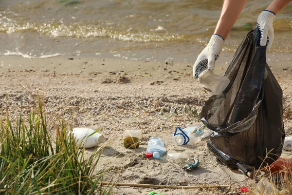 ゴミ袋を持った手袋をした女が浜でゴミを集めて — ストック写真