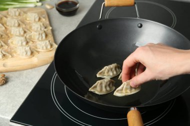 Kadın kızgın yağlı tavaya çiğ gyoza koyuyor, yakın plan.