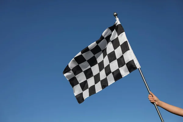 Woman holding checkered finish flag on light blue background, closeup