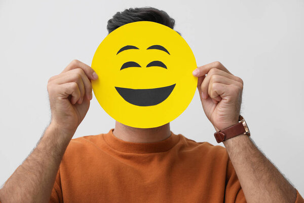 Человек скрывает эмоции с помощью карты с нарисованным улыбающимся лицом на белом фоне