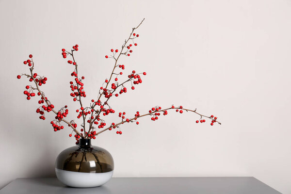 Hawthorn branches with red berries in vase on grey table indoors, space for text