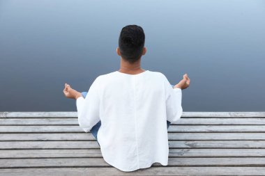 Nehir kenarındaki ahşap iskelede meditasyon yapan bir adam.
