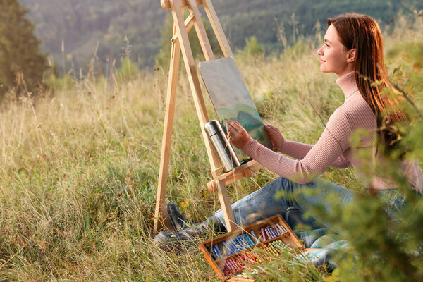 Young woman drawing landscape with soft pastels in nature. Space for text