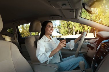 Modern bir arabada oturan bir bardak içkiyle güzel genç bir sürücü.