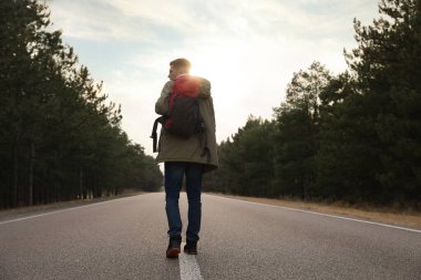 Sırt çantalı bir adam ormanın yakınındaki yol boyunca gidiyor.