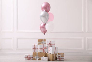 Beyaz duvarın yanında bir sürü hediye kutusu ve balon var.