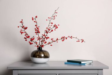 Vazoda kırmızı böğürtlenli Hawthorn dalları ve kapalı alanda gri masa üzerine kitaplar.