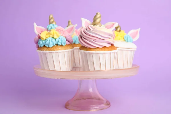 紫の背景を背景に デザートスタンド上のかわいい甘いユニコーンカップケーキ — ストック写真