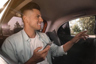Modern taksinin arka koltuğunda akıllı telefonu olan adam.