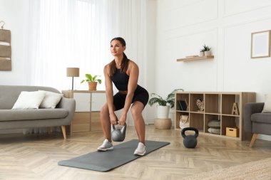 Evde kettlebell ile egzersiz yapan genç bir kadın.