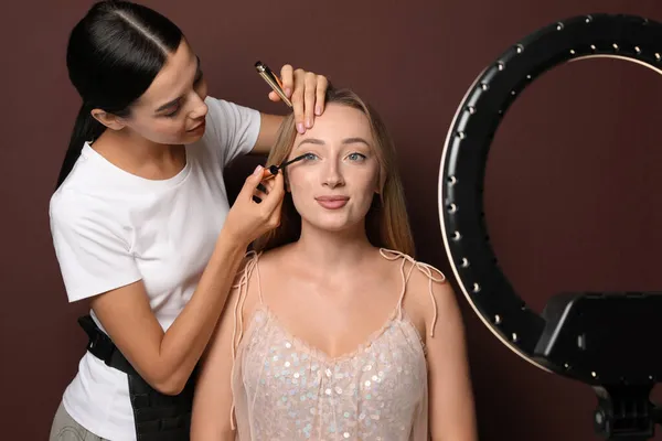 Profesjonalny Makijaż Artysta Pracuje Piękną Młodą Kobietą Brązowym Tle Używanie — Zdjęcie stockowe