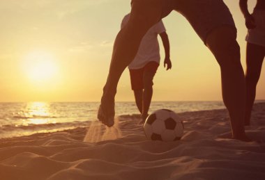Arkadaşlar gün batımında plajda futbol oynuyor, yakın plan.